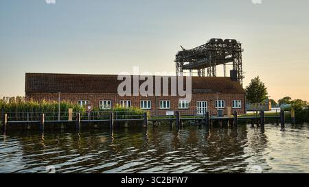 June 12, 2025 – Anklam-Germany: View of old customs office in the harbor, with the remains of the Karnin lift bridge, a landmark in the Peene River. Stock Photo