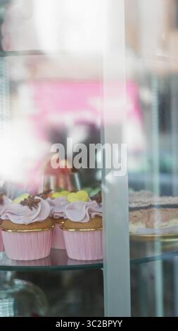 Colorful desserts displayed in a glass case include cupcakes with pink frosting in a bustling cafeteria or bakery setting, offering a vibrant and enti Stock Photo