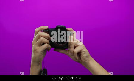 Caucasian man's hands holding a camera against a vibrant pink background, showcasing photography equipment and creativity in an isolated studio settin Stock Photo