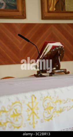 Pulpit with microphone and open bible on altar inside a church setting featuring ornate decorations and framed religious artwork in a serene indoor en Stock Photo
