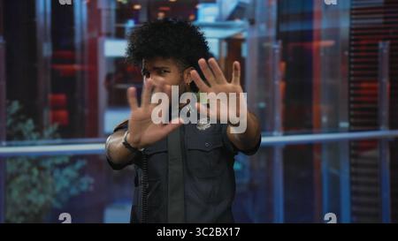 Man in police uniform inside a hotel making stop gesture with both hands against a blurred indoor background. Stock Photo
