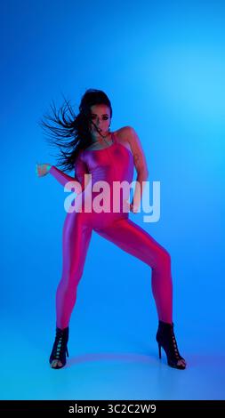 Dancer in pink bodysuit and high heels striking a pose under blue lighting Stock Photo