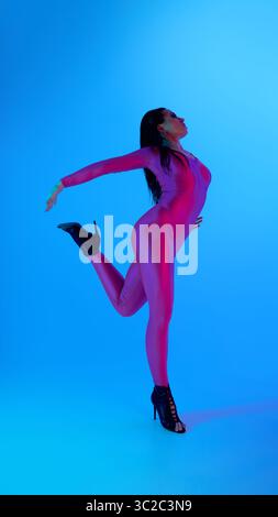 Dancer in vibrant jumpsuit posing elegantly against blue background Stock Photo