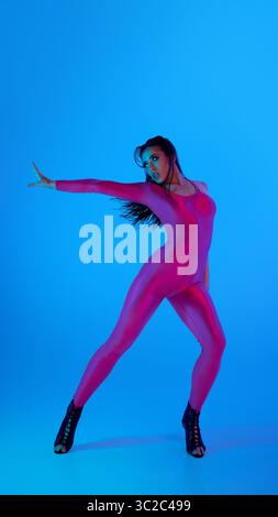 Dancer in vibrant pink bodysuit strikes pose with blue background Stock Photo