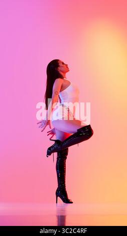 Woman performing in high heels against vibrant orange pink backdrop Stock Photo