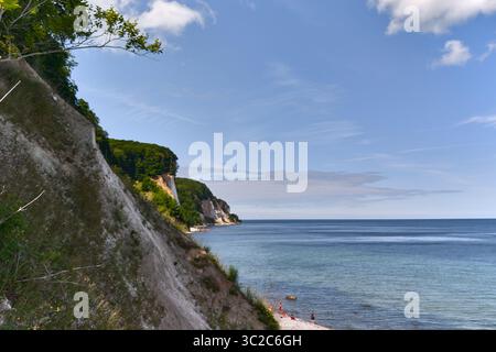 White chalk cliffs near Königsstuhl on Rugen island, Germany. Forested coast meets calm Baltic Sea under a warm summer sky with toursist bathing at be Stock Photo