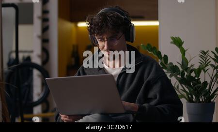 Concentrated Caucasian guy working laptop at home man freelancer programmer chatting website designer in headphones typing online application hipster Stock Photo