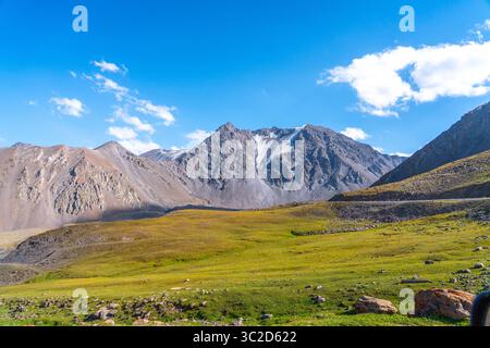 A breathtaking panorama of majestic mountains with snow-capped peaks and vast green valleys under a clear blue sky Stock Photo