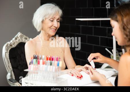 Smiling elderly woman receiving manicure from female manicurist in salon Stock Photo