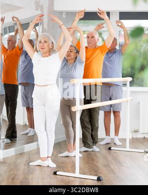 Active mature woman practicing fifth position holding by ballet barre together with others Stock Photo