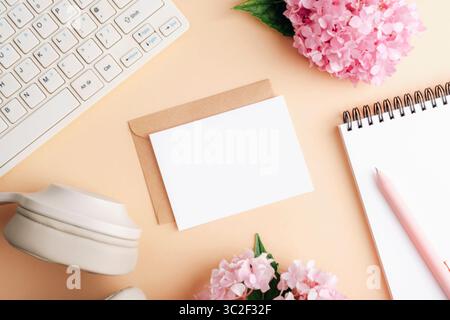 Workplace with envelope, card, notepad and flowers on beige background. Computer keyboard and headphones, concept of working or studying. Top view, fl Stock Photo