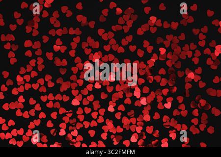 Red glittery heart shaped confetti on a black backdrop. Background pattern. Stock Photo