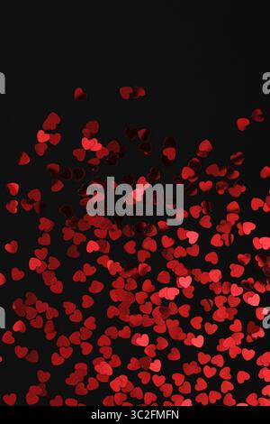 Red glittery heart shaped confetti on a black backdrop. Background pattern. Stock Photo