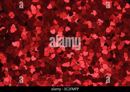 Red glittery heart shaped confetti on a black backdrop. Background pattern. Stock Photo
