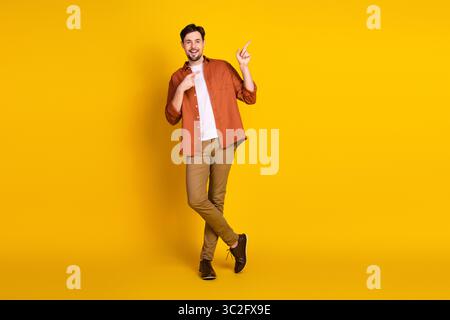 Cheerful young man in casual attire poses on a vibrant yellow background with expressive hand gestures, exuding positivity Stock Photo