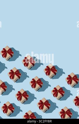 Vertical banner featuring a pattern of brown kraft gift boxes with red velvet bows on a light blue background. Space for your text. Stock Photo