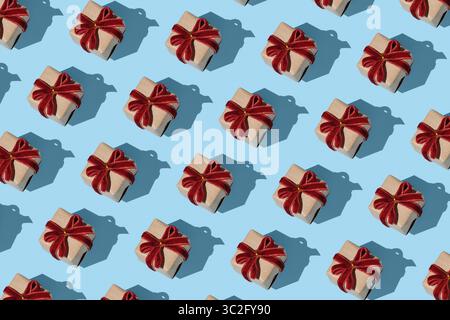 Pattern of brown kraft gift boxes with red velvet bows on a light blue background Stock Photo
