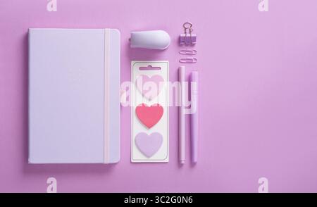 Minimalist pastel stationery flatlay with notepad, stapler, heart shaped stickers, markers, paper clips and pushpins on a lilac background. Place for Stock Photo