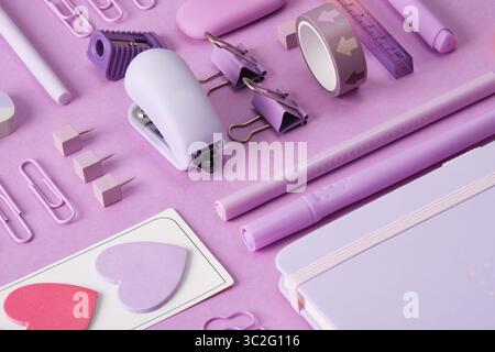 Stationery background with pastel purple supplies, notepad, paper clips, scissors, sticky notes, felt-tip pens, eraser, stapler, ruler, pins. Selectiv Stock Photo