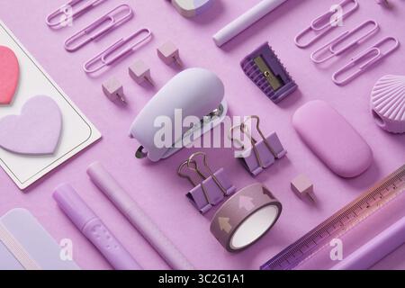Stationery background with pastel purple supplies, notepad, paper clips, stickers, felt-tip pens, eraser, stapler, ruler, pins. Selective Focus. Stock Photo