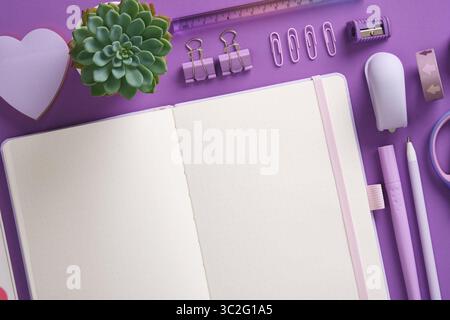 Open notepad and stationery, felt-tip pens, stapler, ruler, eraser, pins, clips in purple theme. Space for your text. Stock Photo