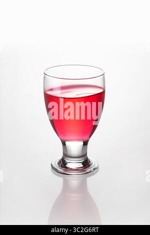 Glencairn type drinking glass containing bright red liquor, isolated on white background with reflection and bokeh Stock Photo