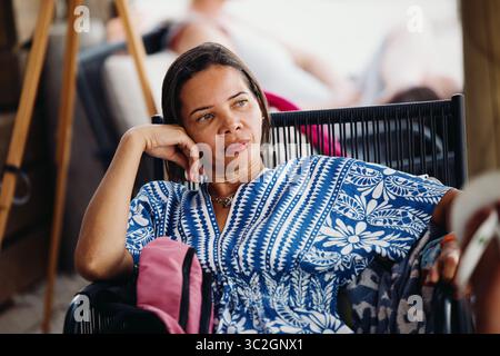 A woman in a bright dress looks thoughtfully into the distance while relaxing at a table in a beach bar. Fazana, Croatia - circa 2025 Stock Photo