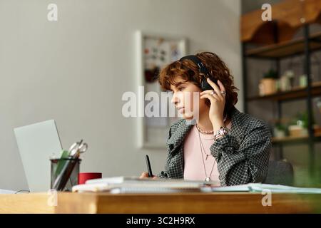Young woman with curly hair engages in remote work from her cozy apartment, focused and productive. Stock Photo