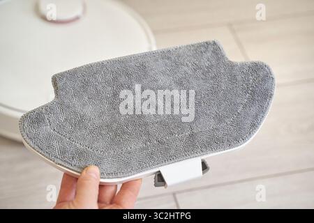 Hand holding microfiber mop pad for robotic vacuum cleaner on light wood floor background. Stock Photo