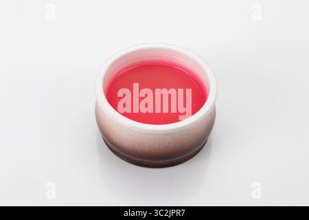 Small round ceramic bowl containing bright red jelly, isolated on white background with reflection and bokeh Stock Photo