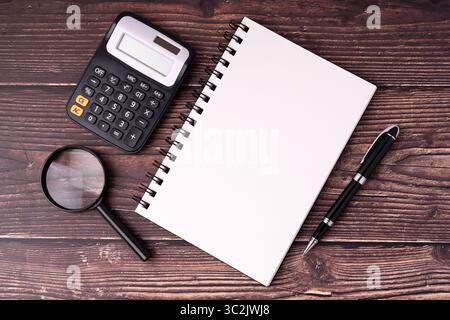 Calculator, blank notepad, magnifying glass and pen on wood background Stock Photo