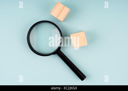 Magnifying glass and two wood blocks on blue background Stock Photo