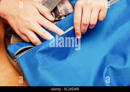 Close-up of blue school bag for papers and documents, hands open lock on backpack Stock Photo