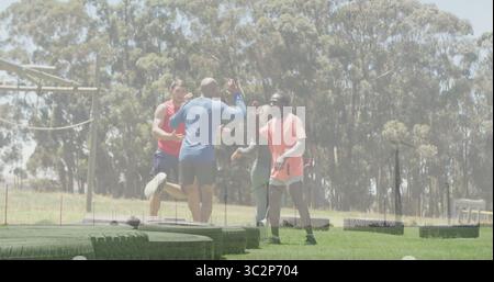 Celebrating group of four adults exchanging high fives on grassy training field, with stacked tires. Athletes, teamwork, outdoor, fitness, motivation, Stock Photo