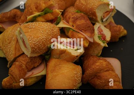 Assorted sandwiches in a black platter, viewed from above. Filled with cheese, lettuce, and deli meats in sesame rolls and croissants. Stock Photo