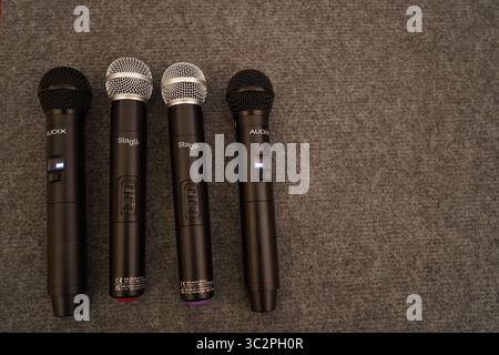 Four wireless handheld microphones by Audix and Stagg, placed on carpet, prepared for use in a conference, live event, or stage presentation Stock Photo