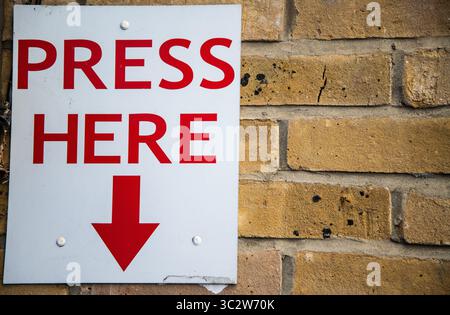 Large "PRESS HERE" sign in bold red letters with a downward-pointing red arrow, mounted on a brick wall. Attention-grabbing signage, possibly for emer Stock Photo
