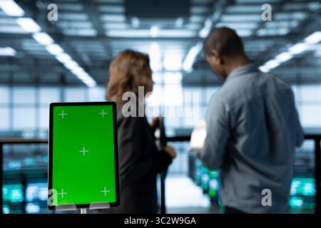 Close up of mockup tablet next to server room data scientists conducting security audits, preventing bugs. Green screen device and african american man with colleague in data center Stock Photo