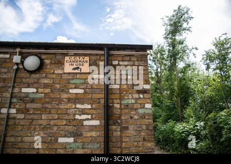 CCTV warning sign with black text on orange background and camera icon, mounted on the side of a brick building, indicating surveillance in operation. Stock Photo