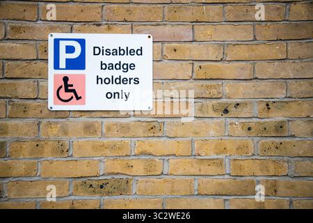 Disabled badge holders only parking sign mounted on a brick wall, indicating restricted parking for blue badge holders in a designated area. Stock Photo