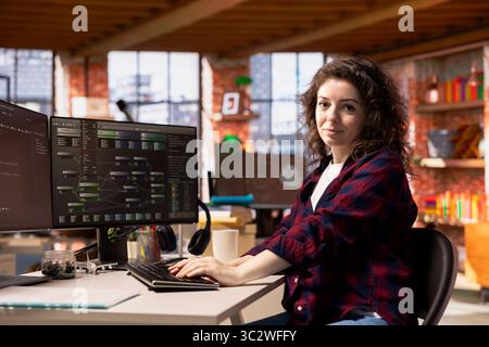 Portrait of smiling programmer coding advanced AI algorithm in startup workspace, refining machine learning models to enhance automation. Happy woman using coding platform in Silicon Valley office Stock Photo