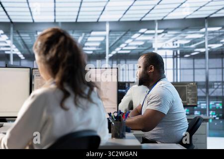 Woman sitting next to african american coworker in data center doing checkup on electronics to avoid downtime. Engineer and colleague supervising server room infrastructure components Stock Photo
