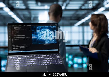 AI technology coding on laptop in data center with programmers in blurry background employing machine learning models. Close up of notebook used by artificial intelligence IT experts Stock Photo