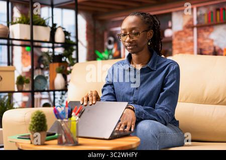 Independent woman using laptop for remote job tasks at home office, doing research and enjoying the benefits of schedule flexibility. Embracing the modern lifestyle of freelance work. Stock Photo