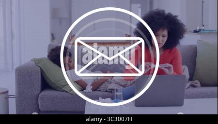Working mother typing on laptop while son using smartphone on grey couch in living room Stock Photo