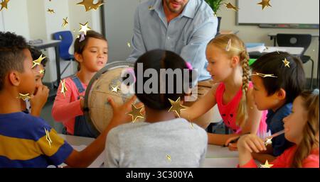 Guiding male teacher and children leaning over globe and pointing at map in classroom, with globe Stock Photo
