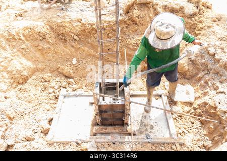 Construction worker pouring concrete into a column foundation formwork using a concrete vibrator to ensure proper compaction. Stock Photo
