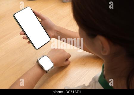 A woman interacts with a smartphone and smartwatch with blank screens, showcasing modern wearable and mobile technology on a wooden desk in a top view Stock Photo