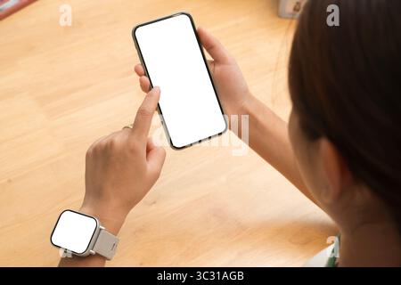 A woman interacts with a blank smartphone screen while wearing a smartwatch, emphasizing smart technology usage, connectivity, and digital lifestyle i Stock Photo