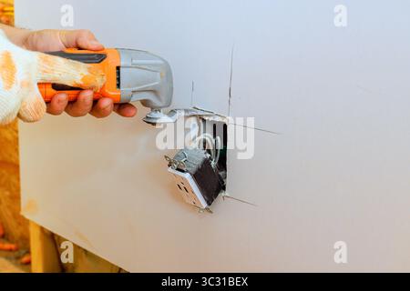 Hand holds power tool, cutting drywall around an electrical outlet during home improvement job. Stock Photo